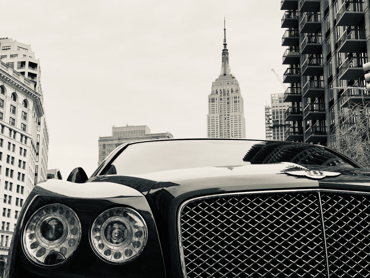 A striking black luxury car set against a bustling cityscape and iconic skyscraper.
